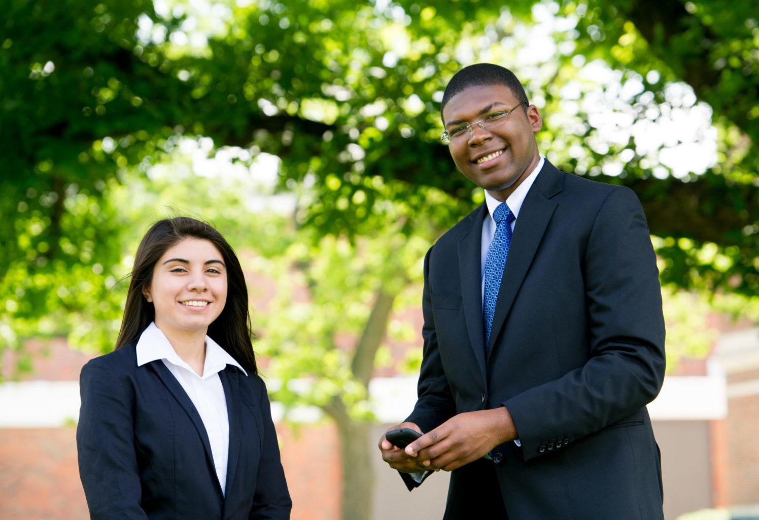 Two students dressed professionally standing outside on campus.