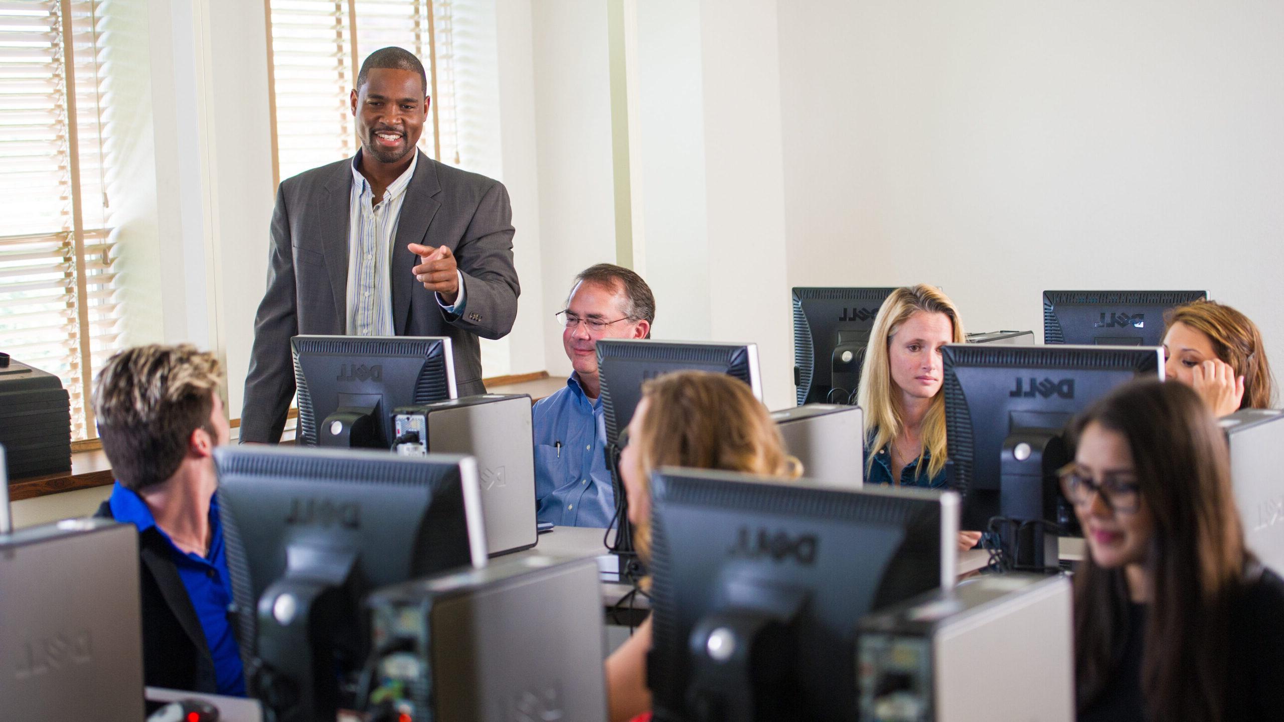 Professor in the computer lab with students sitting down in front of the screens.