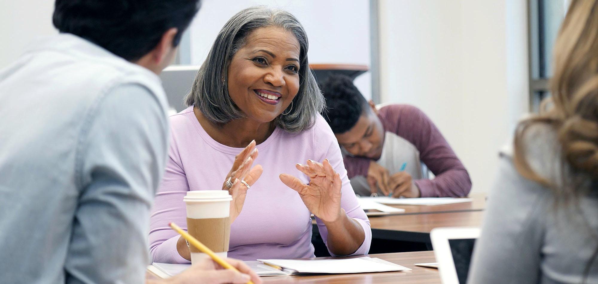 Professional talking with students sitting at a table.